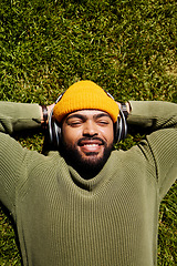 Image showing Top view, headphones and man relax on grass outdoor, listening to music and audio online or hearing sound of podcast. Smile, streaming radio and person at park resting for peace, calm and freedom