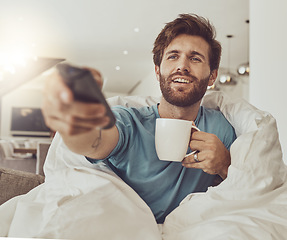 Image showing Coffee, relax and a man in a blanket watching tv on a sofa in the living room of his home for entertainment streaming. Movie, television or subscription with a happy young person using a remote