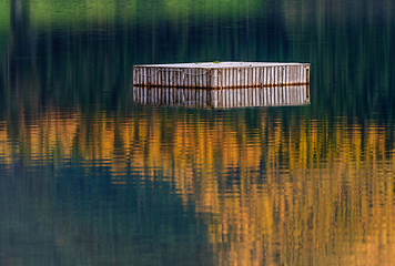 Image showing old wooden raft reflecting in water with autumn colours
