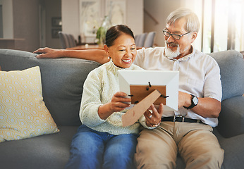 Image showing Elderly couple, happy and together with memory or photograph on sofa with smile in living room. Senior man, woman and married with embrace by sit, bond and love in relationship for vacation, holiday