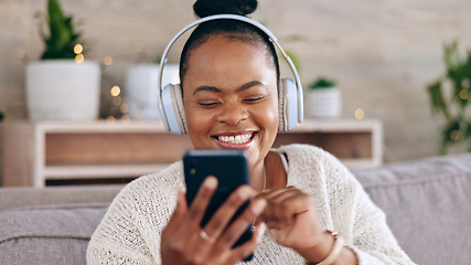 Image showing Black woman, headphones for music and smartphone, relax on couch at home and audio streaming with smile. Happiness, mobile app and using phone for radio or podcast, scroll with technology in lounge