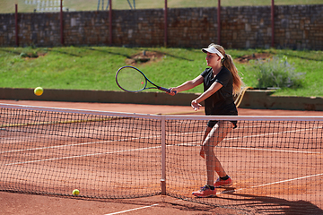 Image showing A young girl showing professional tennis skills in a competitive match on a sunny day, surrounded by the modern aesthetics of a tennis court.