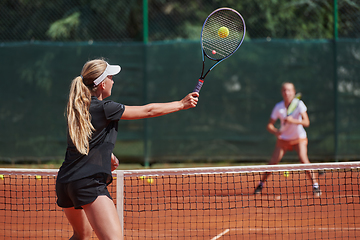 Image showing Young girls in a lively tennis match on a sunny day, demonstrating their skills and enthusiasm on a modern tennis court.