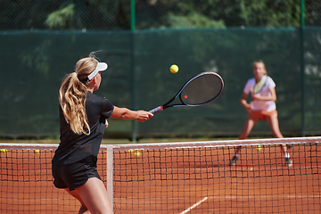 Image showing Young girls in a lively tennis match on a sunny day, demonstrating their skills and enthusiasm on a modern tennis court.