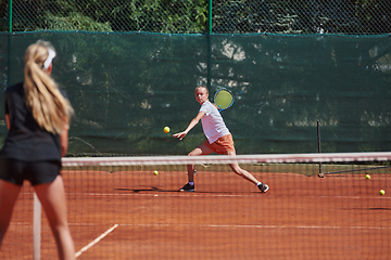 Image showing Young girls in a lively tennis match on a sunny day, demonstrating their skills and enthusiasm on a modern tennis court.