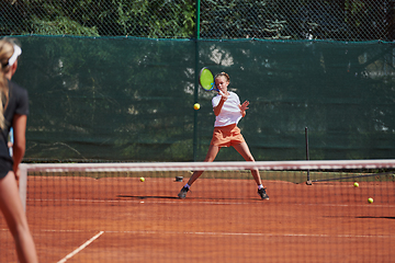 Image showing Young girls in a lively tennis match on a sunny day, demonstrating their skills and enthusiasm on a modern tennis court.