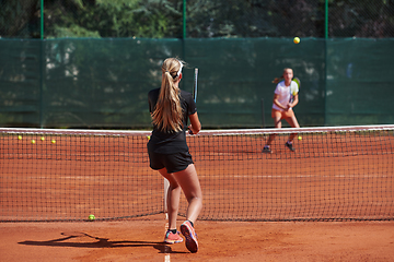 Image showing Young girls in a lively tennis match on a sunny day, demonstrating their skills and enthusiasm on a modern tennis court.