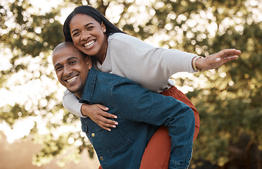 Image showing Couple, park and piggy back with smile, portrait and airplane game in nature, holiday and bonding in summer. Man, woman and playful in backyard, freedom and vacation by trees with love in sunshine