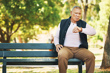 Image showing Check, watch and senior man outdoor in nature, park or planning activity in retirement schedule. Reading, time and elderly person sitting on bench in woods, environment or forest with technology