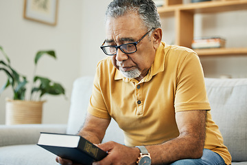 Image showing Man, holding and book in thought at home, memory and alone for comfort in hope. Male, person or grandfather on sofa in living room with thoughts of bible, religion or church in prayer for support