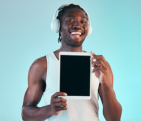 Image showing Headphones, mockup and black man with tablet screen in a studio listening to music, playlist or album. Happy, smile and African male model with digital technology streaming song by blue background.