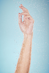 Image showing Water drops, hand and closeup with cleaning, shower and morning dermatology in studio. Blue background, person arm and splash for wellness, washing and skin glow with self care and hygiene safety