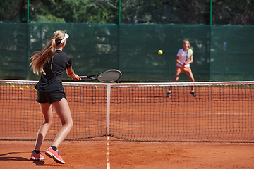 Image showing Young girls in a lively tennis match on a sunny day, demonstrating their skills and enthusiasm on a modern tennis court.