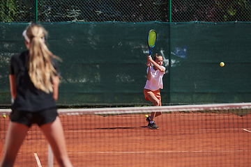 Image showing Young girls in a lively tennis match on a sunny day, demonstrating their skills and enthusiasm on a modern tennis court.