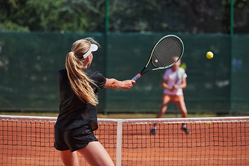 Image showing Young girls in a lively tennis match on a sunny day, demonstrating their skills and enthusiasm on a modern tennis court.