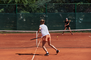 Image showing Young girls in a lively tennis match on a sunny day, demonstrating their skills and enthusiasm on a modern tennis court.