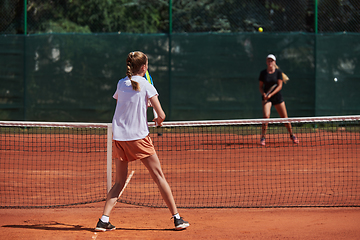 Image showing Young girls in a lively tennis match on a sunny day, demonstrating their skills and enthusiasm on a modern tennis court.