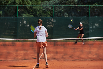 Image showing Young girls in a lively tennis match on a sunny day, demonstrating their skills and enthusiasm on a modern tennis court.