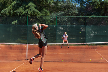 Image showing Young girls in a lively tennis match on a sunny day, demonstrating their skills and enthusiasm on a modern tennis court.