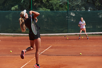 Image showing Young girls in a lively tennis match on a sunny day, demonstrating their skills and enthusiasm on a modern tennis court.