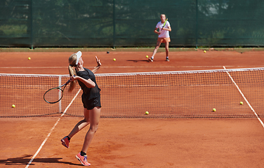 Image showing Young girls in a lively tennis match on a sunny day, demonstrating their skills and enthusiasm on a modern tennis court.