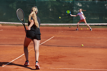 Image showing Young girls in a lively tennis match on a sunny day, demonstrating their skills and enthusiasm on a modern tennis court.