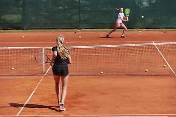 Image showing Young girls in a lively tennis match on a sunny day, demonstrating their skills and enthusiasm on a modern tennis court.