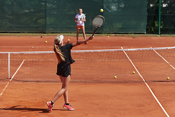 Image showing Young girls in a lively tennis match on a sunny day, demonstrating their skills and enthusiasm on a modern tennis court.