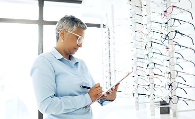 Image showing Doctor, eye care or senior woman with checklist in store for retail stock, inventory or eyewear choice. Vision, ophthalmology or optician in clinic writing on clipboard for product in optometry shop