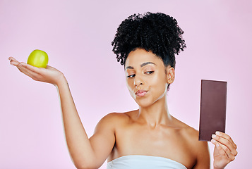 Image showing Woman in studio with apple, chocolate and decision for food, wellness and skincare nutrition. Fruit vs sugar, diet and choice for beauty model on pink background with challenge for healthy eating.
