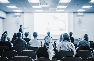 Image showing Speaker giving a talk in conference hall at business event. Rear view of unrecognizable people in audience at the conference hall. Business and entrepreneurship concept. Blue tones black and white.