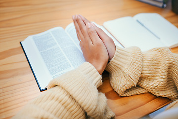 Image showing Hands, bible and praying at desk, religion and Christian worship in home at table. Closeup, holy book and woman in meditation for God, Jesus and Christ for faith in spiritual gospel, praise or hope