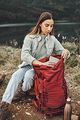 Image showing Woman, hiking and packing backpack in nature with tablet, check and thinking by lake, mountain or outdoor. Girl, luggage and trekking with bad, technology and ideas on adventure in countryside