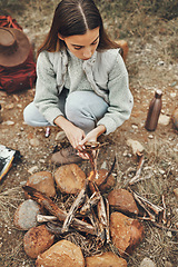 Image showing Wood, nature and woman with fire on a camp on a mountain for adventure, weekend trip or vacation. Stone, sticks and young female person making a flame or spark in outdoor woods or forest for holiday.