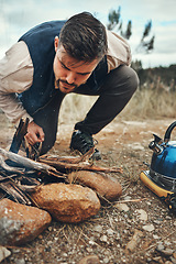 Image showing Wood, nature and man with fire on a camp on a mountain for adventure, weekend trip or vacation. Stone, sticks and young male person making a flame or spark in outdoor woods or forest for holiday.