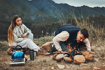 Image showing Wood, mountain and couple with fire on a camp in nature for adventure, weekend trip or vacation. Stone, sticks and young man and woman making a flame or spark in outdoor woods or forest for holiday.