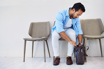 Image showing Man, interview and job in waiting room, chair and looking for cv in bag by wall background. Business person, recruitment and marketing opportunity or vacancy, human resources and hiring for position