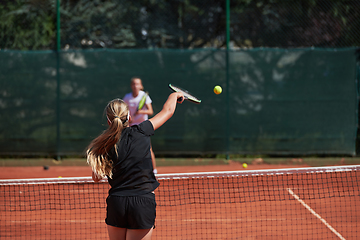 Image showing Young girls in a lively tennis match on a sunny day, demonstrating their skills and enthusiasm on a modern tennis court.