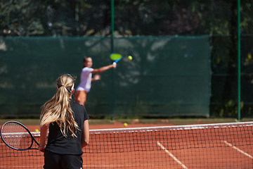 Image showing Young girls in a lively tennis match on a sunny day, demonstrating their skills and enthusiasm on a modern tennis court.