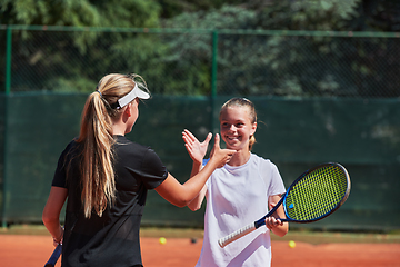 Image showing Two female tennis players shaking hands with smiles on a sunny day, exuding sportsmanship and friendship after a competitive match.