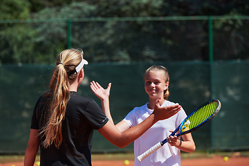 Image showing Two female tennis players shaking hands with smiles on a sunny day, exuding sportsmanship and friendship after a competitive match.