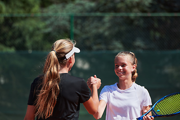 Image showing Two female tennis players shaking hands with smiles on a sunny day, exuding sportsmanship and friendship after a competitive match.