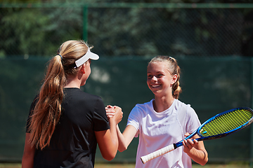 Image showing Two female tennis players shaking hands with smiles on a sunny day, exuding sportsmanship and friendship after a competitive match.