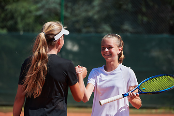 Image showing Two female tennis players shaking hands with smiles on a sunny day, exuding sportsmanship and friendship after a competitive match.