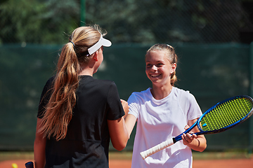 Image showing Two female tennis players shaking hands with smiles on a sunny day, exuding sportsmanship and friendship after a competitive match.