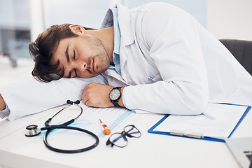 Image showing Healthcare, tired and a doctor man sleeping at his desk in the hospital with fatigue or exhaustion. Medical, burnout and an overworked young medicine professional asleep in his office at the clinic