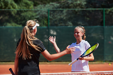 Image showing Two female tennis players shaking hands with smiles on a sunny day, exuding sportsmanship and friendship after a competitive match.