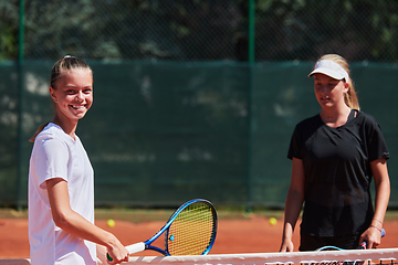 Image showing Two female tennis players shaking hands with smiles on a sunny day, exuding sportsmanship and friendship after a competitive match.