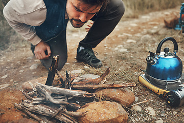 Image showing Wood, nature and man with fire on camp for kettle on an outdoor adventure, vacation or weekend trip. Stones, sticks and young male person blowing for flame or smoke in the forest on holiday in Canada
