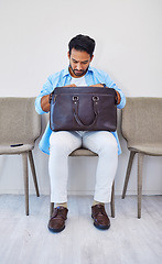 Image showing Interview, man and job in waiting room, briefcase and looking for cv in bag by wall background. Business person, search and anxious to find resume, human resources and hiring or marketing opportunity